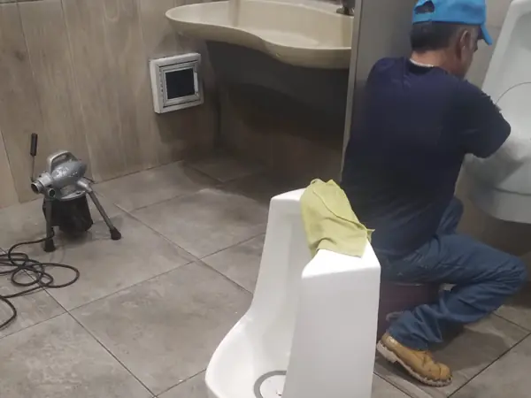 Plomero metiendo la sonda en un mingitorio de un baño comercial